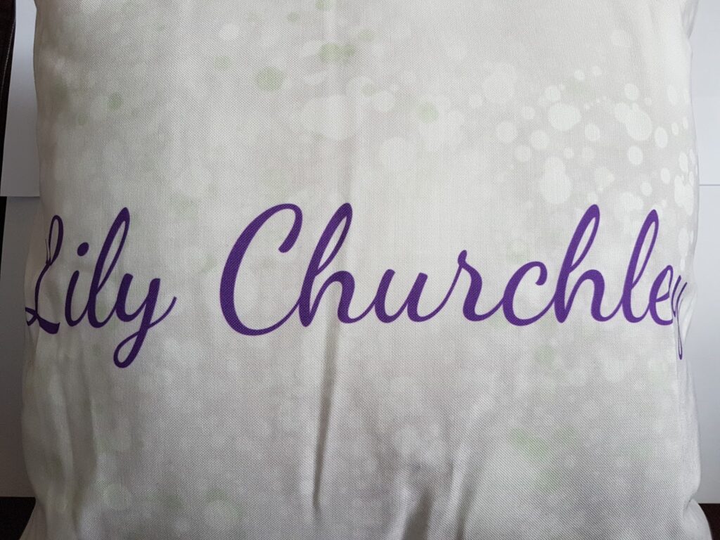 A white pillow with a subtle light green and white bubble pattern features the name "Lily Churchley" written across it in large, flowing purple script.