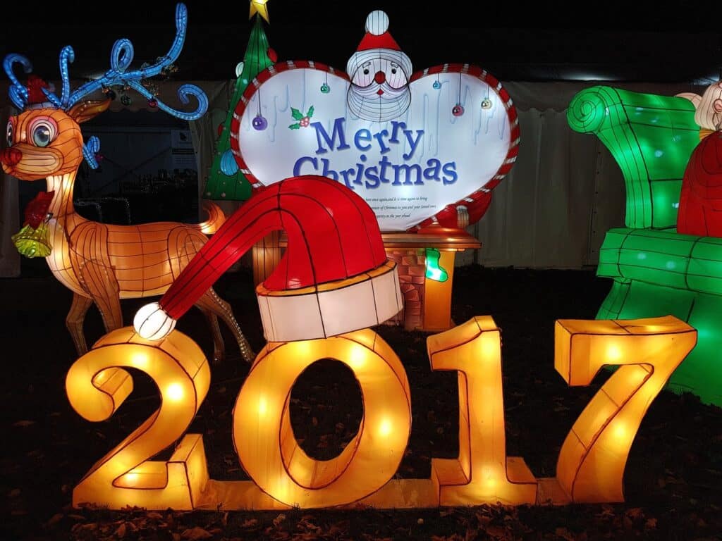 A festive light display shows a large illuminated "2017" with a Santa hat on the "0." Behind it, a reindeer and a cheerful Father Christmas stand by a heart-shaped sign that reads "Merry Christmas." Bright, colourful lighting creates a holiday atmosphere at night.