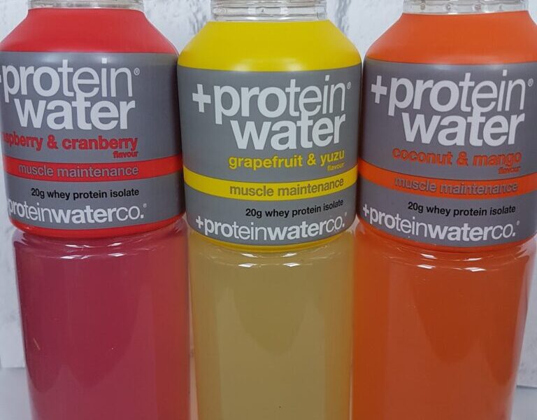 Three bottles of +Protein Water are side by side. Flavours are raspberry & cranberry (pink), grapefruit & yuzu (yellow), and coconut & mango (orange). Each label highlights "muscle maintenance" and "20g whey protein isolate.