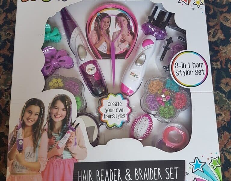 A boxed “Be U” Hair Beader & Braider Set for ages 5+, showing pink and white hair styling tools, colourful hair beads, combs, elastics, and accessories. The packaging features two smiling girls and text: “Create your own hairstyles” and “3-in-1 hair styler set.”.