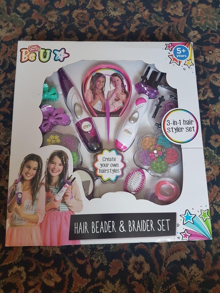 A boxed “Be U Hair Beader & Braider Set” for ages 5+, featuring tools and colourful hair accessories. The white box displays images of two smiling girls and includes the text “Create your own hairstyles!” and “3-in-1 hair styler set” on the front.