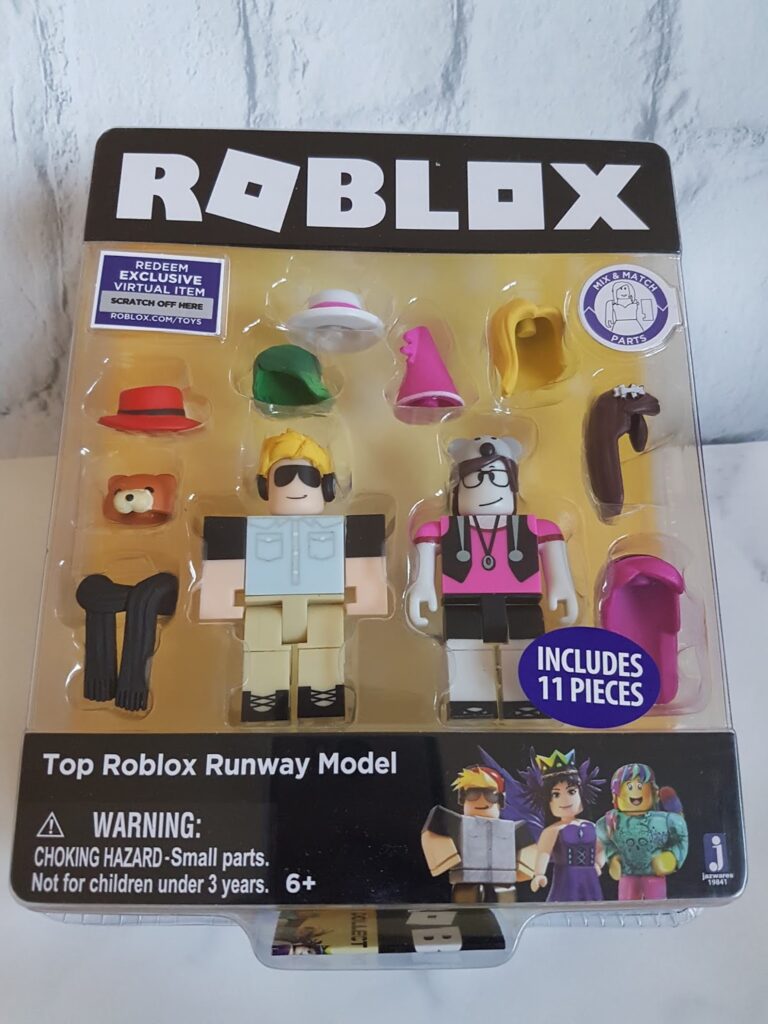 A packaged Roblox toy set titled “Top Roblox Runway Model,” featuring two blocky figures with interchangeable hats, glasses, and accessories. The packaging displays 11 pieces, a warning about small parts, and is recommended for ages 6 and over.