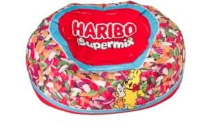 A colourful bean bag designed with images of assorted Haribo sweets, featuring a red area at the top with the white text "HARIBO Supermix" and a cartoon bear holding sweets on the side. The background is white.