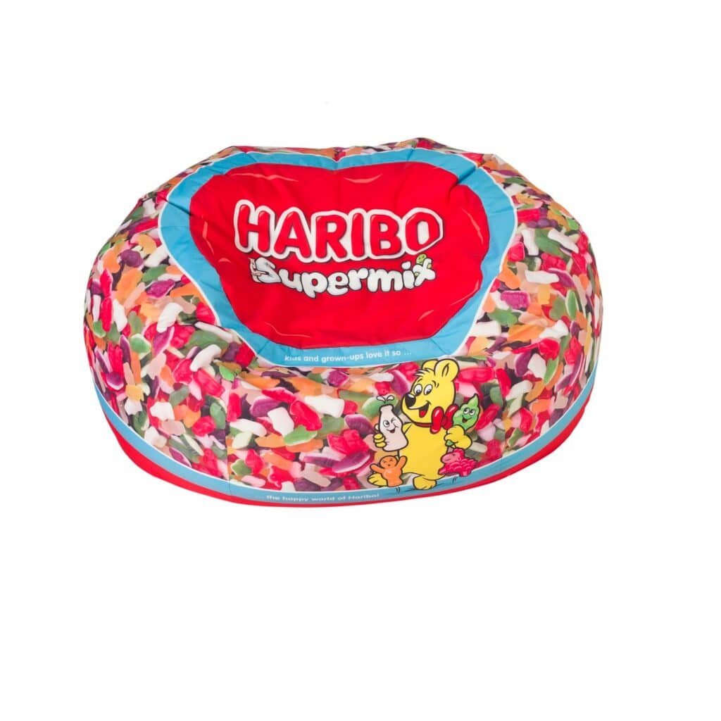 A colourful bean bag chair with a Haribo Supermix theme. The top features a large red label with "HARIBO Supermix" in white letters, surrounded by images of assorted gummy sweets and the Haribo bear mascot holding sweets. The background is white.