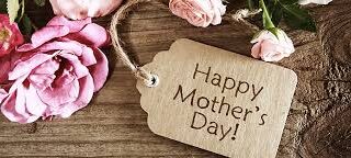 A rustic wooden surface with a bunch of pink roses and a brown gift tag tied with string. The tag has the words “Happy Mother’s Day!” written on it in large, clear letters. The scene feels warm and celebratory.