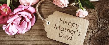 A rustic wooden surface with a bunch of pink roses and a brown gift tag tied with string. The tag has the words “Happy Mother’s Day!” written on it in large, clear letters. The scene feels warm and celebratory.