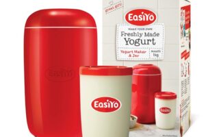 A red Easiyo yoghurt maker, a white jar with a red lid and Easiyo logo, and a product box showing the same items. The box reads “Freshly Made Yoghurt,” mentions it makes 1kg, and displays images of yoghurt and fruit.