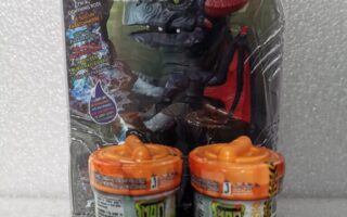 A toy dragon named Shockwave in its packaging is displayed upright behind two orange-and-green Mad Lab Untamed toy canisters. The packaging shows the dragon’s face and details, with age recommendation icons and warnings on both the box and canisters.