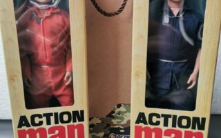 Two boxed Action Man dolls stand upright. The left box is labelled “Action Pilot” and contains a figure in a red jumpsuit with a white helmet. The right, “Action Sailor,” wears a navy uniform and cap. Behind them is a gift bag reading “#1 Dad”.