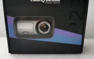 A black box for a Nextbase Dash Cam model 222 is displayed upright on a textured white surface. The box features an image of the dash cam with a prominent lens and a blue and purple diagonal stripe behind it.