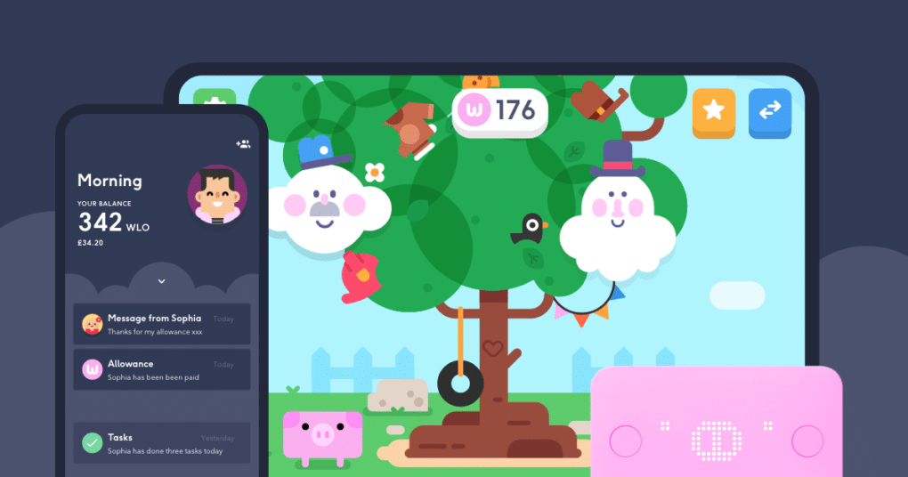 A colourful cartoon scene shows a big tree with playful faces, animals, and objects, displayed on a tablet. In front, a mobile phone screen shows messages, balance details, and tasks. A pink card and piggy bank icon are also visible, suggesting a financial app for children.