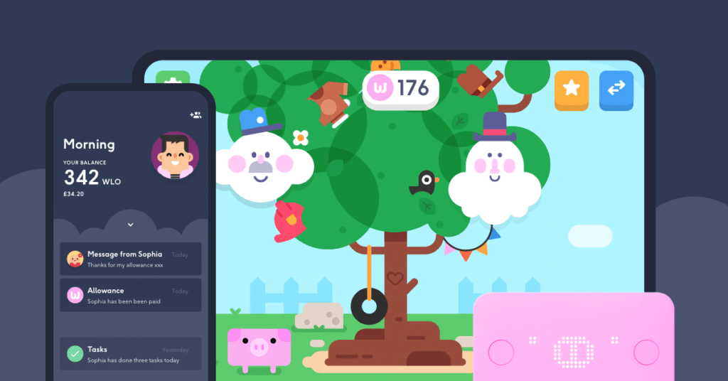A colourful cartoon scene shows a big tree with playful faces, animals, and objects, displayed on a tablet. In front, a mobile phone screen shows messages, balance details, and tasks. A pink card and piggy bank icon are also visible, suggesting a financial app for children.