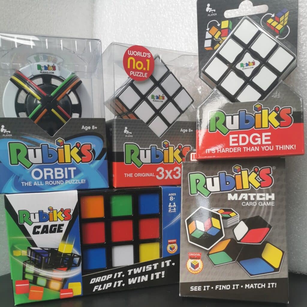 A display of Rubik’s products including Rubik’s Orbit, 3x3 cube, Edge, Cage, and Match card game, all in their packaging. The packages are colourful, featuring images of the puzzles, logos, and various promotional text.