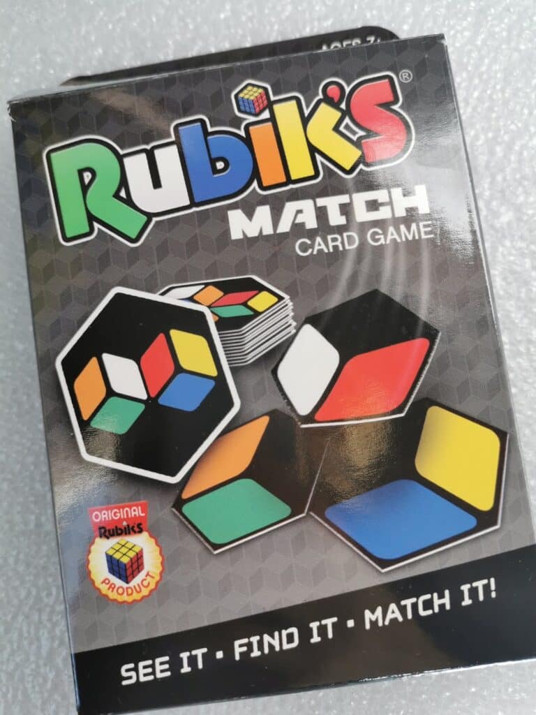 Box of Rubik’s Match Card Game. The front shows the game name and logo, several hexagonal cards with Rubik’s Cube colour patterns, and the strapline, “SEE IT • FIND IT • MATCH IT!” An “Original Rubik’s Product” seal appears in the lower left corner.