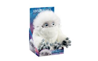 A soft toy of a white yeti with big blue eyes, grey face, and large grey hands sits in a colourful "Abominable" film-themed display box. The box features snowy mountain graphics and the word "Abominable" in bold blue letters at the bottom.