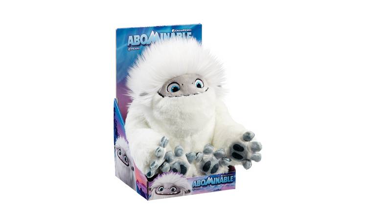 A soft toy of a white yeti with big blue eyes, grey face, and large grey hands sits in a colourful "Abominable" film-themed display box. The box features snowy mountain graphics and the word "Abominable" in bold blue letters at the bottom.