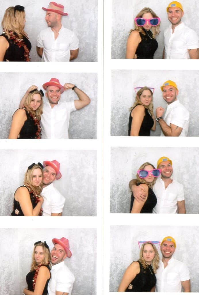 A man in a white shirt and a woman in a black dress pose in a photo booth. They wear various hats, sunglasses, and cat ear headbands, making playful faces and gestures against a light grey backdrop in eight different photos.