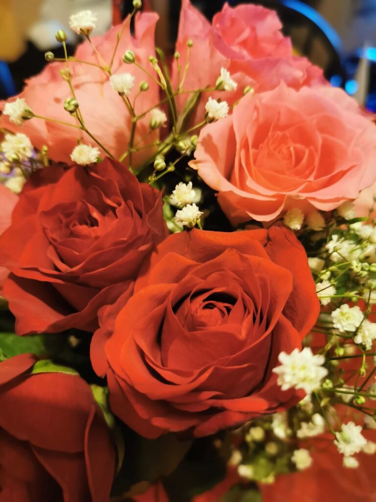 A close-up of a bouquet featuring red and pink roses accented with delicate white baby's breath flowers. The petals are vibrant, and the flowers are arranged closely together, creating a lush and romantic display.