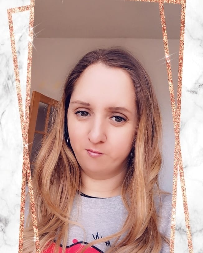A woman with long, wavy blonde hair and fair skin looks at the camera with a slight smile. She wears a light grey shirt. The image has a marble and rose gold glitter border with sparkling accents. The background is an indoor setting.