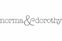 The image features the text “norma & dorothy” in a lowercase, thin, grey serif font. The ampersand is slightly larger and more decorative than the other letters, creating a stylish and elegant look. The background is plain white.
