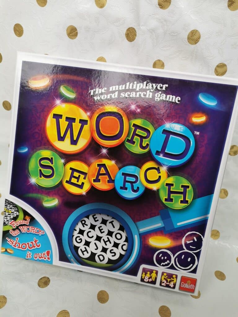 A game box for "Word Search" is shown against a white background with gold dots. The colourful title is large, with letters in circles. The tagline reads “The multiplayer wordsearch game.” Icons at the bottom show it's for 2–4 players and ages 7+.