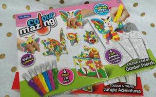 A “Colourmazing” craft kit box features colourful butterflies and animals, paint pens, and completed craft samples. The label highlights “Blend colours,” “6 magic ink pens,” “4 crafts to decorate & display,” and “Colour & Create Garden Friends.”.