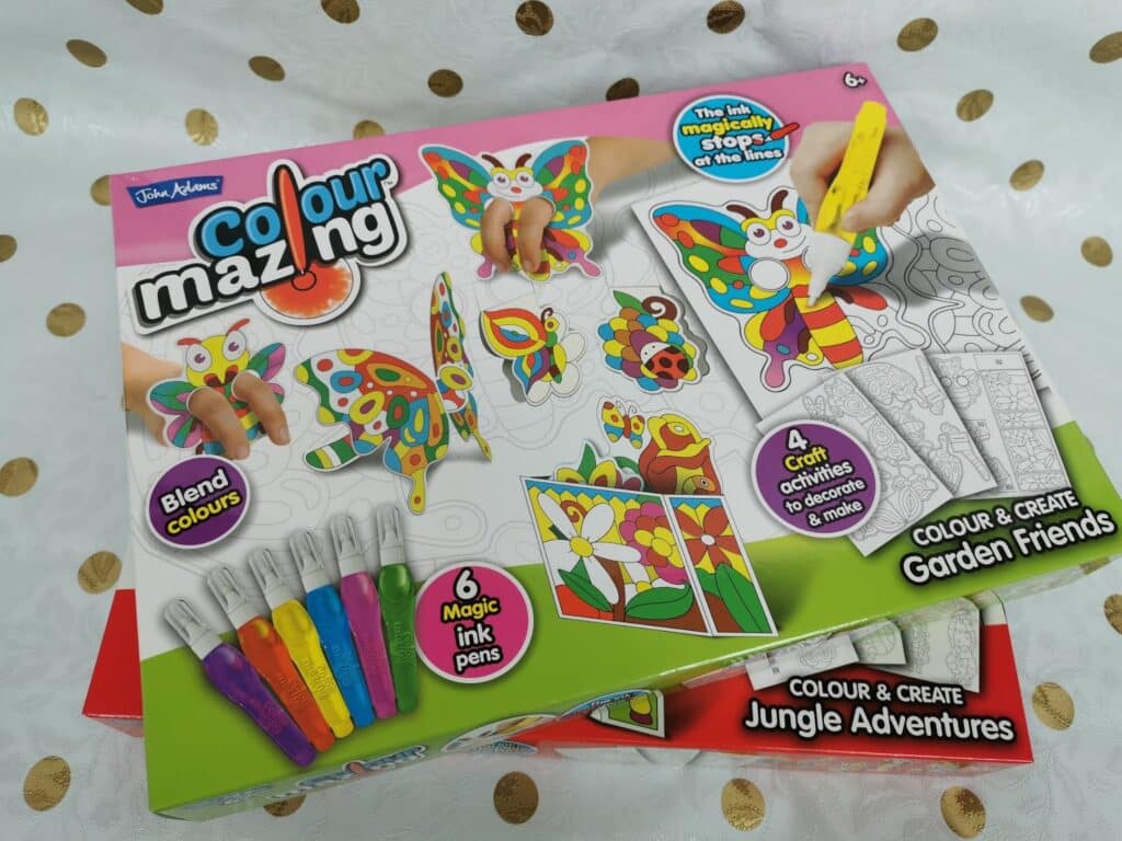 A Colourmazing craft kit box features colourful butterflies, flowers, and markers. Text reads: “Blend colours," "6 magic ink pens," "4 crafts," and "Colour & Create Garden Friends.” The open box reveals illustrated card pieces to colour.