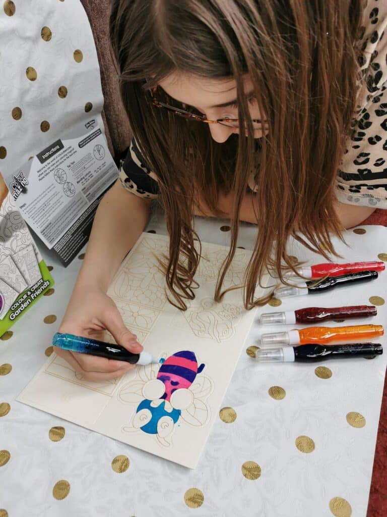 A girl drawing on a piece of paper with felt-tip pens.