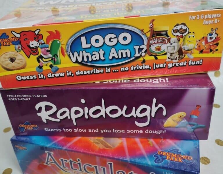 Three colourful board game boxes are stacked. The top box is "LOGO What Am I?"; the middle is "Rapidough" showing playdough and a hand; the bottom is "Articulate! For Kids." The background is white with gold polka dots.
