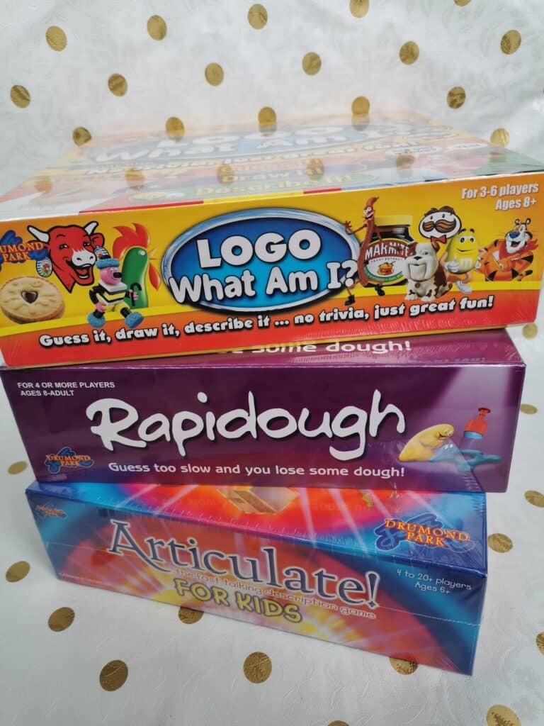 A close-up of three colourful board game boxes stacked on a gold polka dot background: "Logo What Am I?" on top, "Rapidough" in the middle, and "Articulate! For Kids" at the bottom. Each box shows playful branding and age recommendations.
