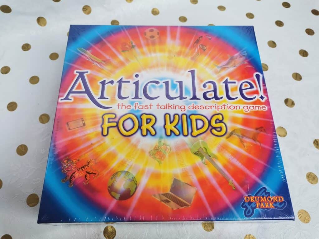 A brightly coloured Articulate! For Kids board game box is shown. The background features a vibrant spiral of red, yellow, blue, and orange, with images of objects like a football, guitar, and laptop. The Drummond Park logo is in the bottom right corner.