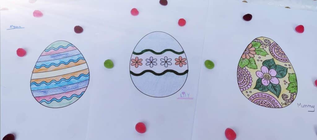 Three sheets of paper each display a large Easter egg drawing, coloured with different patterns: stripes, flowers with wavy lines, and intricate floral designs. The papers are surrounded by colourful round sweets. Names “Ryan,” “Ivy,” and “Mummy” are written on each sheet.