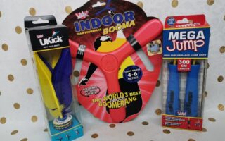 Three toys in packaging on a dotted background: a UKick shuttlecock (yellow, blue, black), a red foam Indoor Booma boomerang labelled “WORLD’S BEST INDOOR BOOMERANG,” and a blue Mega Jump high performance skipping rope, 300 cm length.
