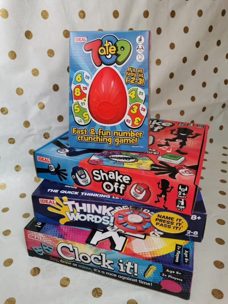 A stack of four colourful Ideal brand board games on a gold polka dot background: Totem, Shake Off, Think Words!, and Clock It!. The Totem game box, featuring a red plastic totem, is placed upright on top of the pile.