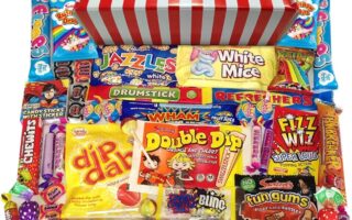 A red and white striped box sits open, overflowing with assorted colourful retro sweets, including Wham bars, Refresher chews, Dip Dab, Drumstick, Fizz Wiz, White Mice, Fun Gums, candy sticks, lollipops, and other treats, all neatly arranged in front.