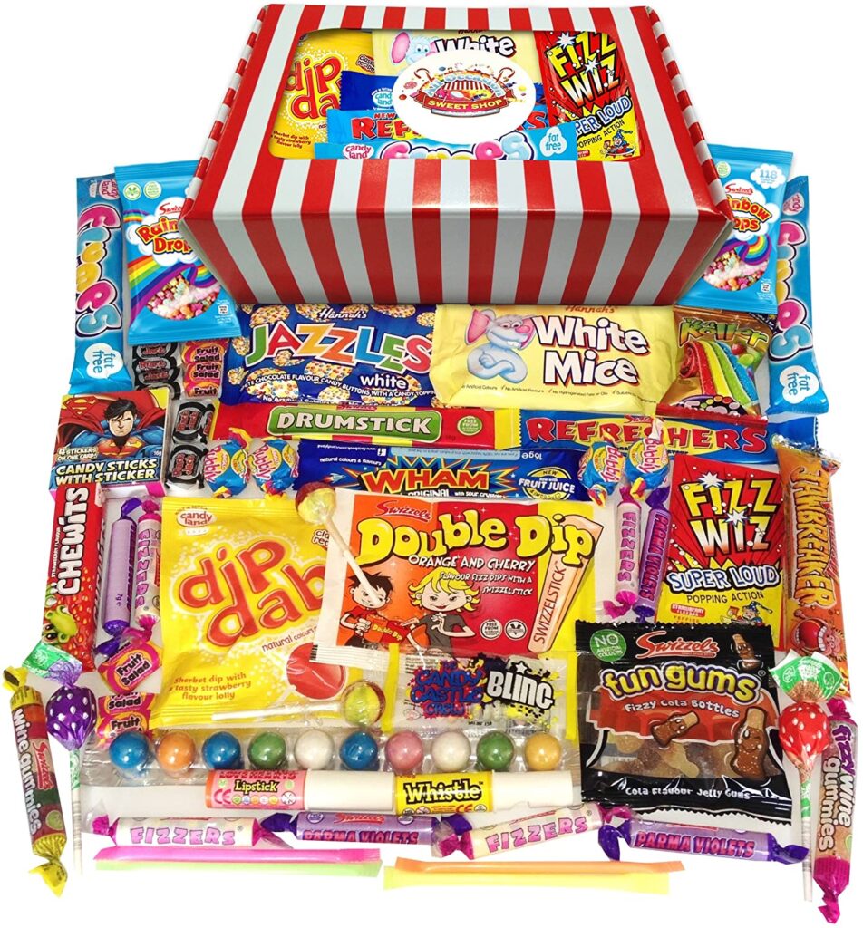 A colourful assortment of retro British sweets is displayed in front of a red and white striped gift box. Visible treats include Dip Dab, Refresher bars, Fizz Wiz, Drumstick, white mice, Jazzles, Fun Gums, Wham bar, lollipops, candy sticks, and gumballs.