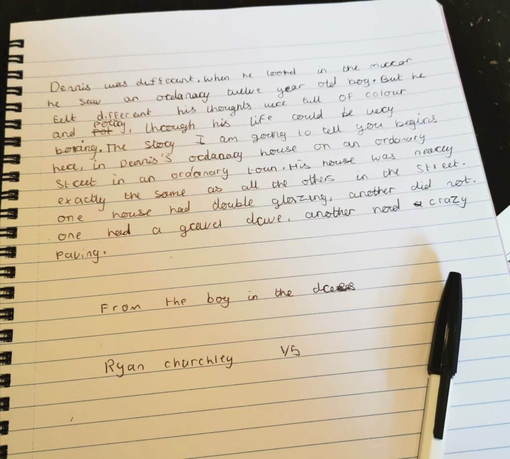 A handwritten story on lined paper is visible. A black-and-white pen rests on the page. The story describes a character named Dennis and his observations about houses. Below, “From the boy in the class” and “Ryan Churchill 7G” are written.