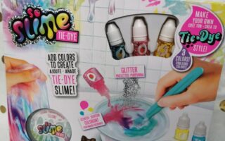 The image shows a colourful So Slime Tie-Dye Slime Kit box. The packaging features paint splashes, slime illustrations, bottles of dye, a mixing bowl with a blue spoon, and text promoting tie-dye, stretchy, glittery, and clear transparent slime.