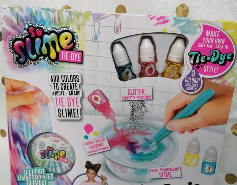 The image shows a colourful So Slime Tie-Dye Slime Kit box. The packaging features paint splashes, slime illustrations, bottles of dye, a mixing bowl with a blue spoon, and text promoting tie-dye, stretchy, glittery, and clear transparent slime.
