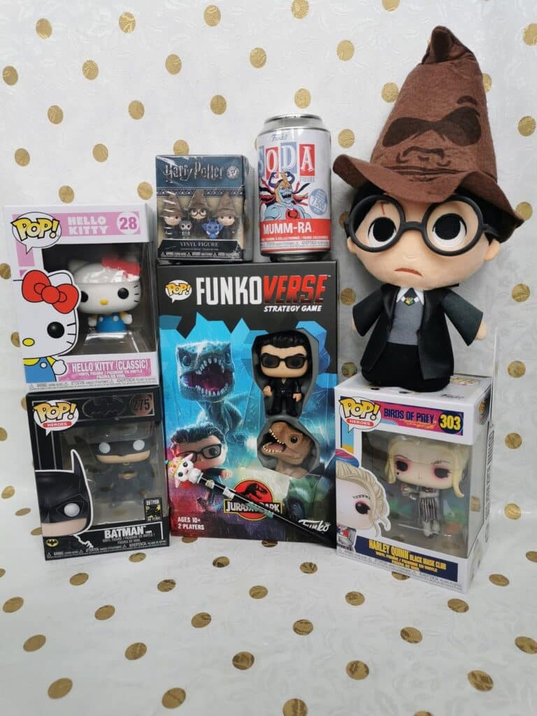 A collection of pop culture items including Funko Pop! figures of Hello Kitty, Batman, and Harley Quinn, a plush Harry Potter doll with a Sorting Hat, a Mumm-Ra figure, a Harry Potter figure, and a Funkoverse Jurassic Park strategy game box.