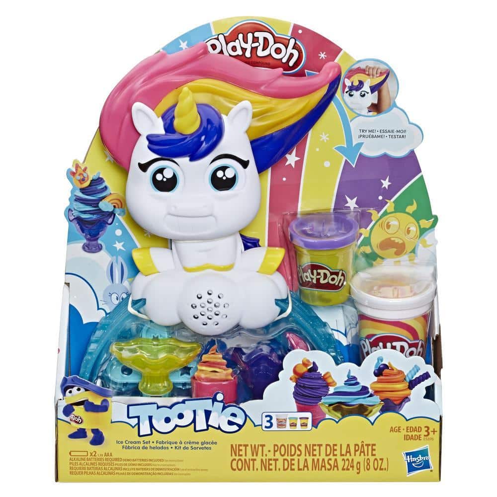 Play-Doh Tootie the Unicorn playset in colourful packaging. Tootie has a rainbow mane, large eyes, and a cheerful expression. Included are three Play-Doh pots and accessories. The background shows rainbows, stars, and Play-Doh creations. For ages 3 and over.