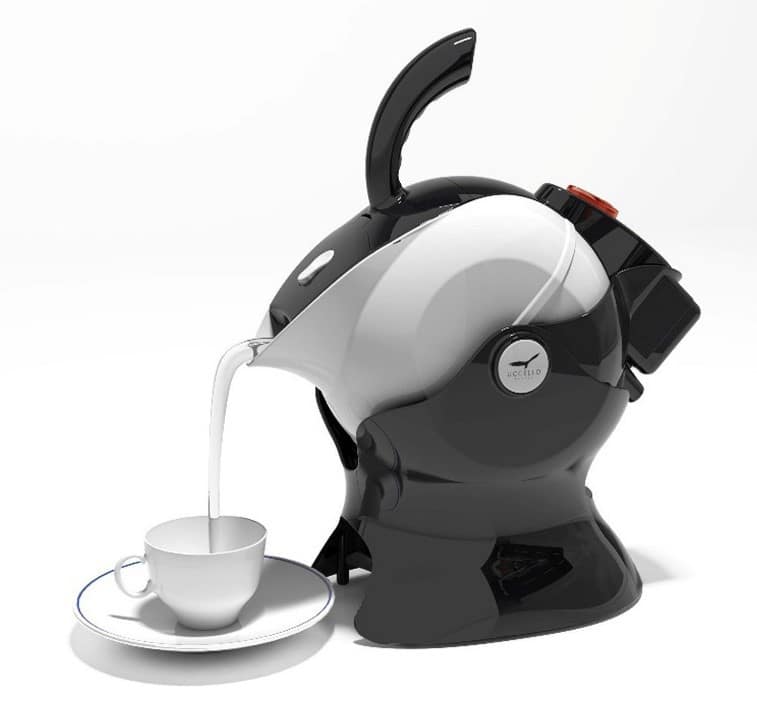 A futuristic, black and white electric kettle shaped like a sculpted helmet pours milk or hot liquid into a white teacup on a saucer. The design is modern and glossy, contrasting with the plain, bright background.