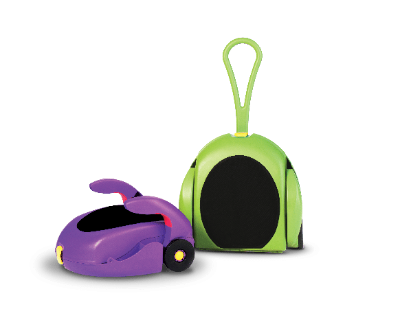 A purple, toy-like suitcase with yellow wheels and an open top sits beside a green suitcase standing upright. Both have oval black panels and are designed with playful, rounded shapes; the green case has a large, looped handle. Background is light grey.