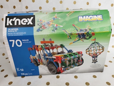 A K’NEX 70 Model Building Set box features colourful K’NEX constructions, including a green, blue, and red car and a spinning ride. The box indicates 705 pieces, suitable for ages 7–12, and has "IMAGINE" in a comic-style bubble.