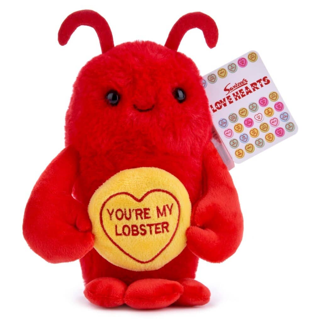 A plush red lobster toy with a smiling face holds a yellow heart embroidered with “YOU’RE MY LOBSTER.” The lobster has two antennae, black eyes, and red claws. A tag attached says “Love Hearts” with colourful heart illustrations.