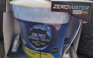 A ZeroWater 12-cup water filter jug is shown in its box, featuring 5-stage advanced filtration. The packaging highlights “Zero Dissolved Solids,” includes a total dissolved solids meter, and mentions certification to reduce lead. The jug is blue and white.