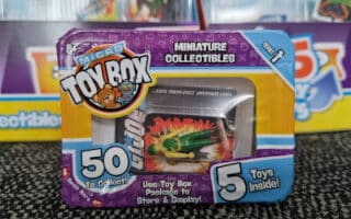 A close-up of a Micro Toy Box package featuring a tiny green toy car inside. The purple packaging highlights “Miniature Collectables,” “50 to collect!,” and “5 toys inside!” with cartoon graphics and a clear window showing the toy.