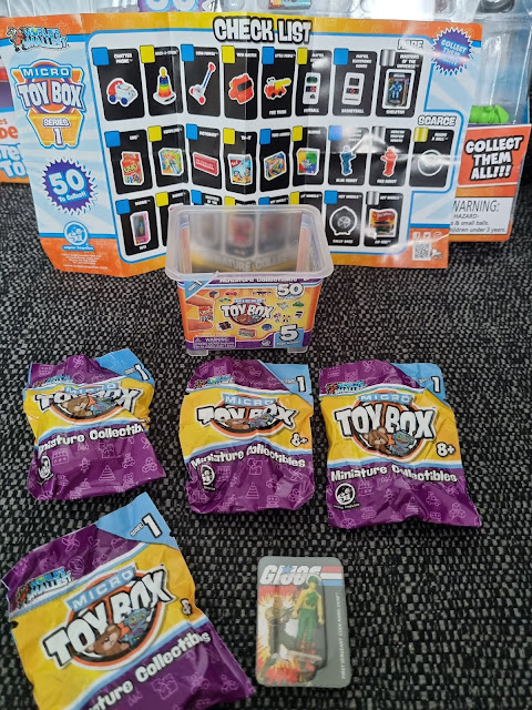 A set of Micro Toy Box miniature collectables is displayed. Five unopened purple toy bags and one plastic tub are in front of a checklist showing all possible toys. A small collectable card with “G.I. Joe” and a figure is at the front on a dark patterned surface.