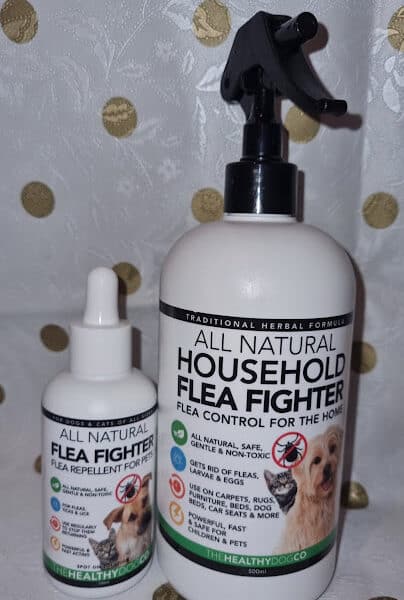 Two bottles of flea treatment products are shown. The smaller dropper bottle is labelled "All Natural Flea Fighter Flea Repellent for Pets." The larger spray bottle reads "All Natural Household Flea Fighter, Flea Control for the Home" with a dog pictured on the label.