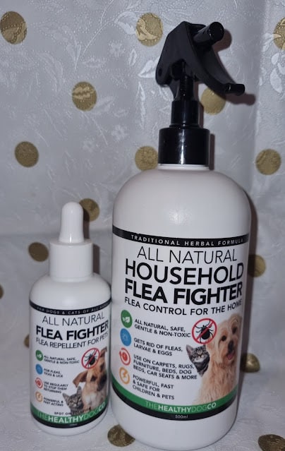 Two bottles of flea treatment products are shown. The smaller dropper bottle is labelled "All Natural Flea Fighter Flea Repellent for Pets." The larger spray bottle reads "All Natural Household Flea Fighter, Flea Control for the Home" with a dog pictured on the label.